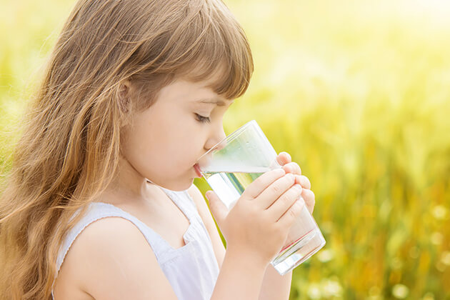 ילדה שותה מים צלולים בכוס מים.